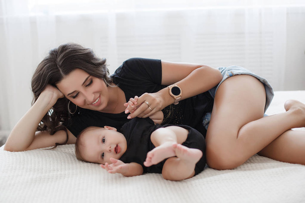 Mother and child on a white bed.Mom and baby boy in shorts playing in sunny bedroom. Parent and little kid relaxing at home.Family having fun together. Bedding and textile for infant nursery.Happy lfamily. Mother playing with her baby in the bedroom - Foto, immagini
