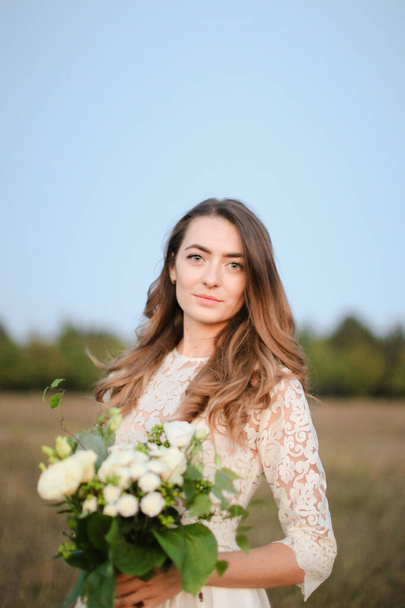 Caucasian beautiful bride with white bouquet background in steppe background. - Zdjęcie, obraz