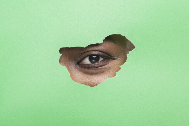 schwarzes Frauenauge ohne Wimperntusche beim Blick durch zerrissenes grünes Papier - Foto, Bild