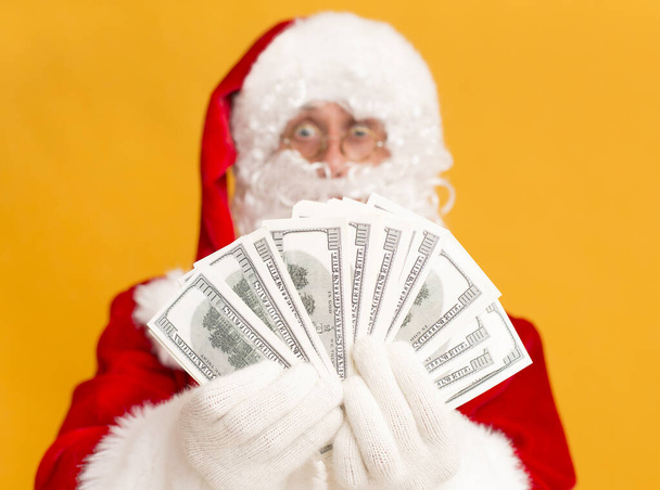 Rich Santa Claus showing many dollar banknotes on orange - Foto, Imagen