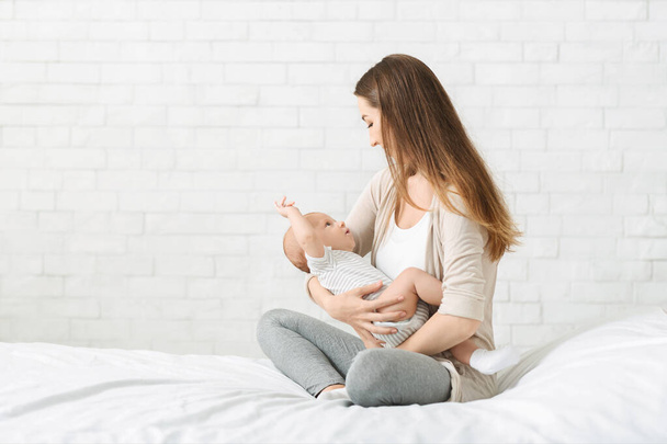 Jovem mãe sentada na cama com bebê recém-nascido nos braços
 - Foto, Imagem