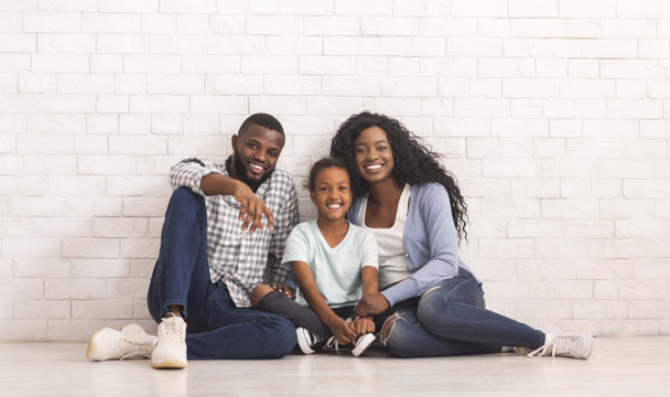 Счастливая чернокожая семья с маленькой дочкой, сидящей на полу вместе
 - Фото, изображение