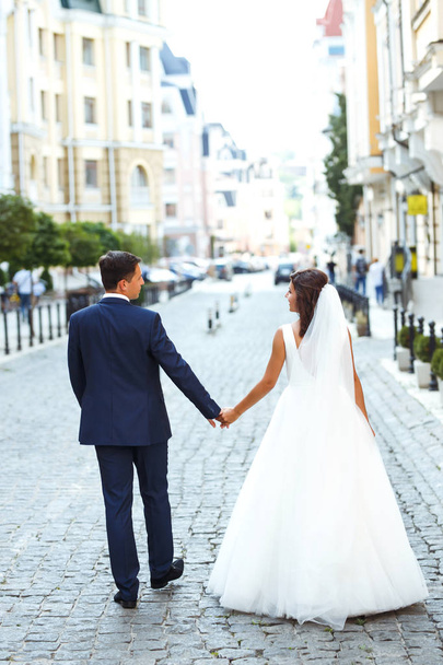 Gorgeous wedding couple walking in the city. Groom in a stylish suit and bride in a beautiful white dress, the couple is walking the streets of the city on their wedding day. Together. Wedding concept - 写真・画像