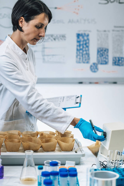 Maaperän näytteet testaus laboratorio. Lähikuva kuva naispuolinen tiedemies yllään valkoinen takki muistiinpanoja laboratoriossa
 - Valokuva, kuva
