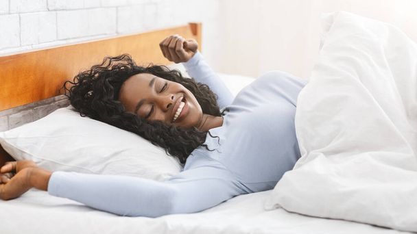 Szczęśliwa afrykańska młoda kobieta rozciągająca się w łóżku - Zdjęcie, obraz
