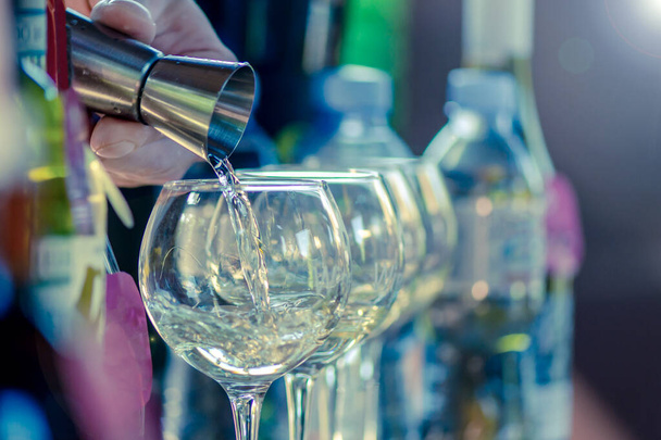 барменская рука с помощью дозатора наливает алкогольный напиток в стакан
 - Фото, изображение
