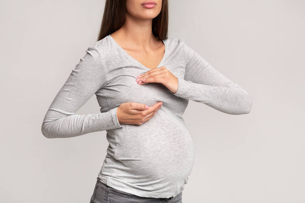 乳痛立ち、灰色の背景に苦しんでいる認識できない妊娠中の女性 - 写真・画像