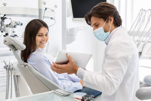 Врач-стоматолог показывает пациенту результат лечения на цифровом планшете
 - Фото, изображение