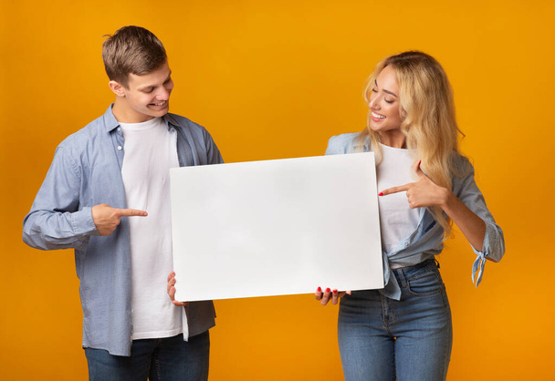 Millennial couple holding blank advertising board and pointing on it - Photo, Image