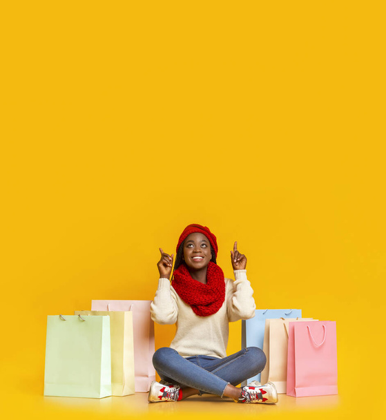 Amazed black girl with purchases pointing up at empty space - Photo, Image
