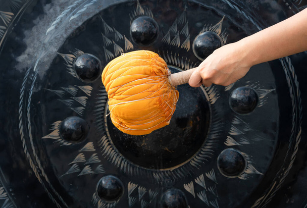 Mano golpeando un gong de metal religioso con un mazo naranja en un templo budista asiático
 - Foto, imagen