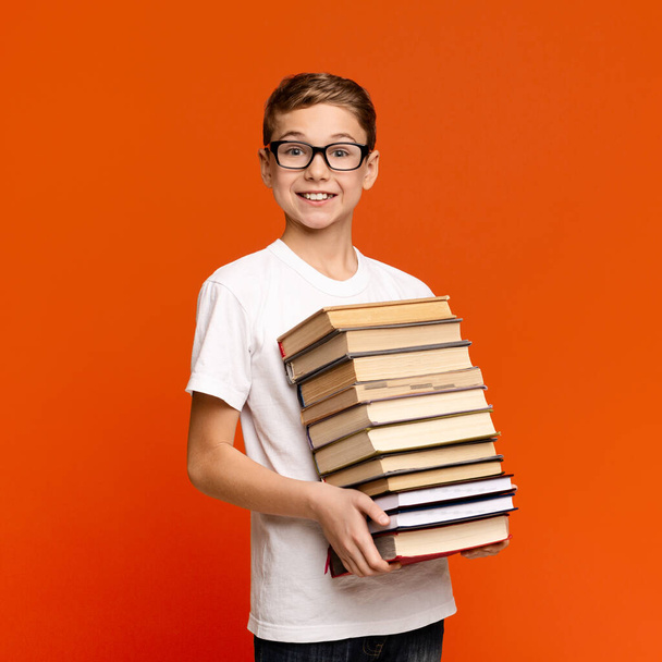 Έξυπνο έφηβο αγόρι με γυαλιά που κρατάει μια στοίβα βιβλία. - Φωτογραφία, εικόνα