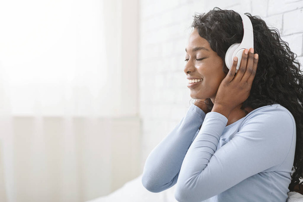 Вид сбоку на афро-девушку с закрытыми глазами, слушающую музыку
 - Фото, изображение