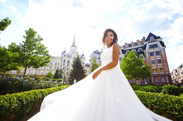 Young  elegant  bride in a white dress in the city. Beautyful  bride with luxury make-up and hairstyle. Happy newlywed woman. Smiling bride. Wedding day. Fashion bride. - Фото, изображение