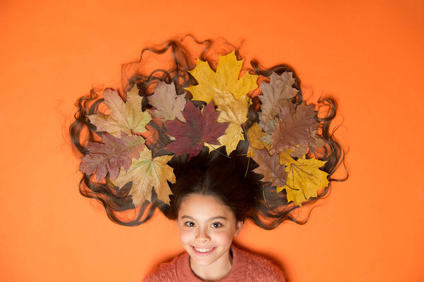 Creative way to wear autumn leaves. Little child with colorful leaves in long brunette hair. Autumn hair care. Care of hair in fall. Autumnal look of small hair model - Photo, image