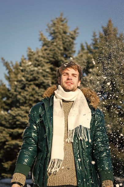 Winter fashion concept. Guy enjoy sunny winter day. Hipster walk snowy winter day. Snowflakes in air on bright winter day. Man unshaven wear warm jacket with fur and scarf snowy nature background - Photo, image