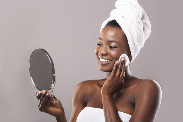 Mulher olhando no espelho e rosto de limpeza com almofada de algodão
 - Foto, Imagem