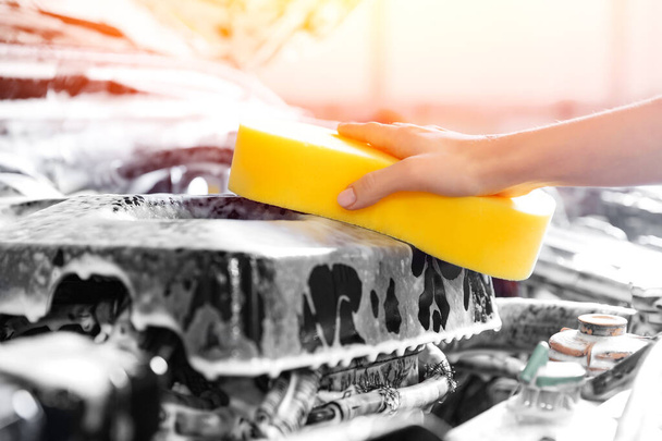 Auton palvelun yksityiskohdat pesu, tyttö käsi keltainen sieni pyyhkimällä moottori uuden ajoneuvon
 - Valokuva, kuva