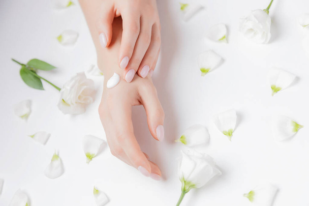 Woman applying hand cream flowers on white background, top view. Concept cosmetic body care, anti-wrinkles, anti-aging spa - Photo, Image