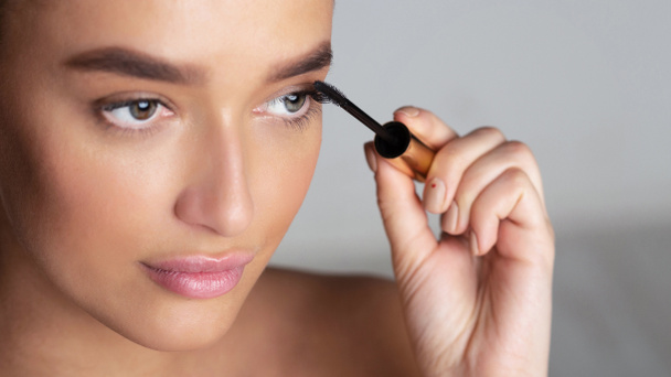 Beautiful millennial woman applying mascara on eyelashes - Photo, Image