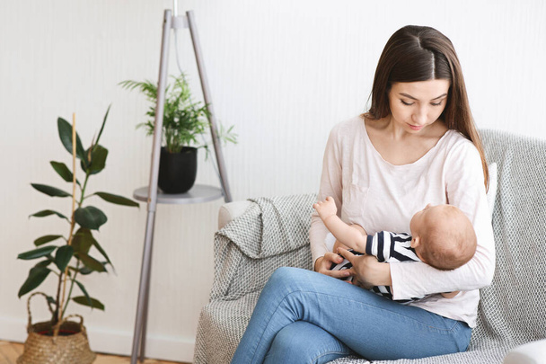 Young mom sitting on couch with newborn baby on hands - Фото, зображення