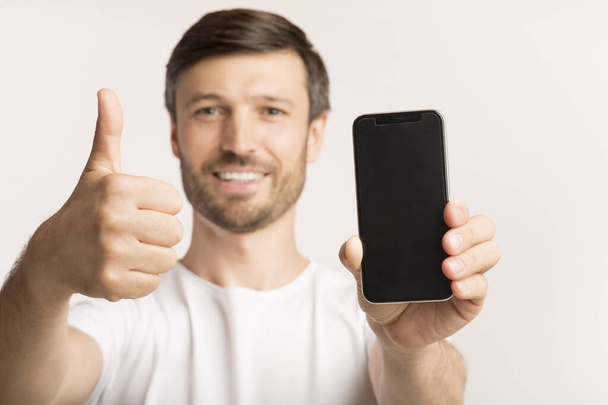 Man Holding Cellphone With Empty Screen Gesturing Thumbs-Up In Studio - Foto, afbeelding