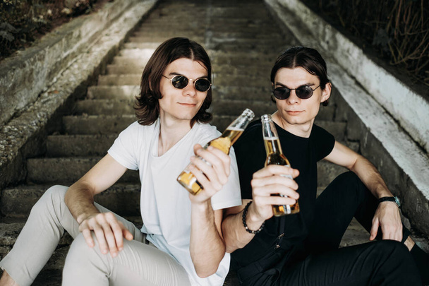 Twee stijlvolle tweeling broers hebben plezier drinken bier op de trappen - Foto, afbeelding