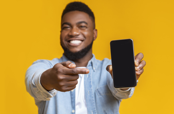fröhlicher Afrikaner zeigt auf Smartphone mit schwarzem Bildschirm - Foto, Bild