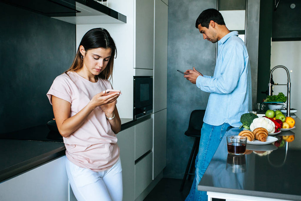 Image of amazing young loving couple at the kitchen have a breakfast using mobile phones - Foto, Imagen
