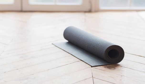 Rolled up yoga mat on wooden floor - Photo, image