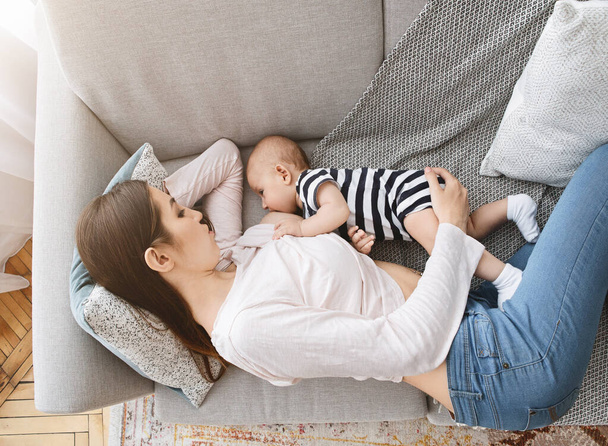 Γυναίκα θηλάζει το παιδί της, ενώ βρίσκεται στον καναπέ στο σπίτι - Φωτογραφία, εικόνα