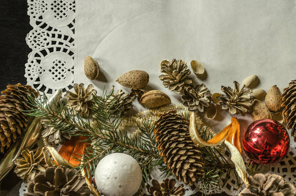 Bottom edge of the openwork paper napkin with various pine cones, fir branch,Christmas toys, almonds and orange peel  - Фото, зображення