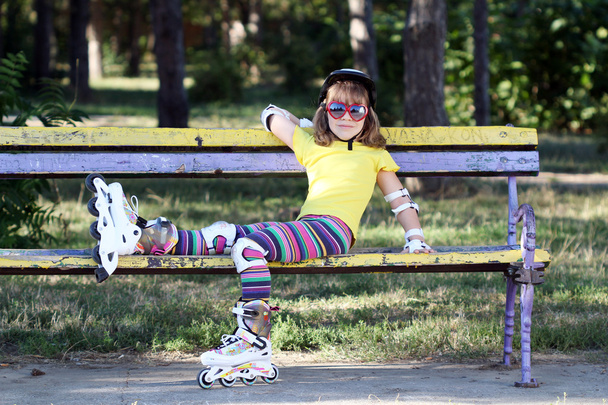 κοριτσάκι με πατίνια και κράνος κάθεται σε παγκάκι - Φωτογραφία, εικόνα