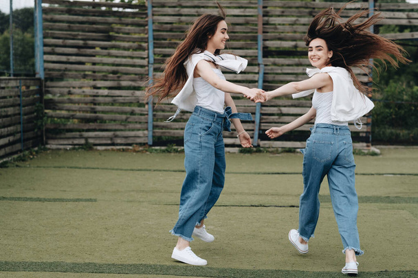 Portrait of Two Young Brunette Twins Sisters Dressed Alike in Jeans and White T-shirt, Best Friends Forever Concept - Foto, Imagen