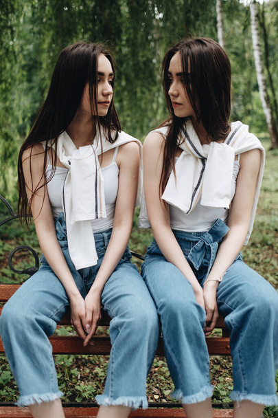Portrait of Two Young Brunette Twins Sisters Dressed Alike in Jeans and White T-shirt, Best Friends Forever Concept - 写真・画像