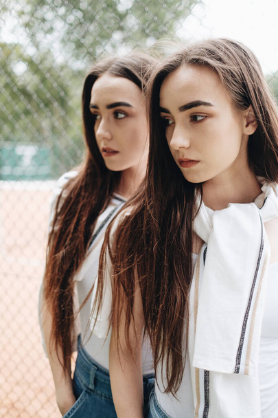 Portrait of Two Young Brunette Twins Sisters Dressed Alike in Jeans and White T-shirt, Best Friends Forever Concept - Photo, Image