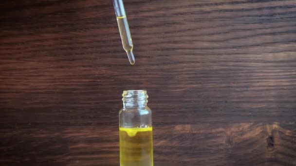 Close-up view of holding the pipette full with essential oil above the bottle and droplets are falling inside. On the wooden background. - Footage, Video
