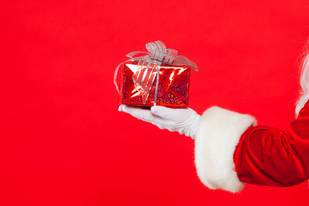Foto der handschuhten Weihnachtsmann-Hand mit Geschenkbox, auf rotem Hintergrund. Weihnachten - Foto, Bild