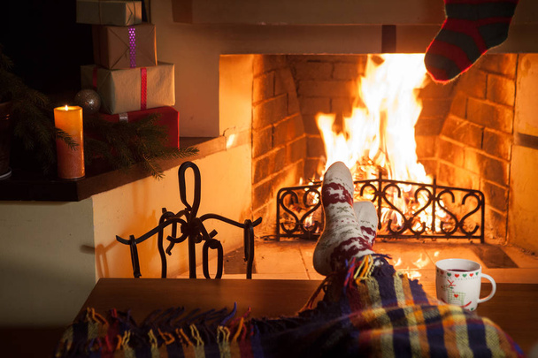Man and woman in warm socks near the fireplace. Cup with a hot drink. Heart. - 写真・画像