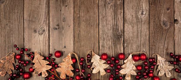Christmas border banner with wood tree decorations and red baubles. Above view on an aged wood background. - Photo, Image