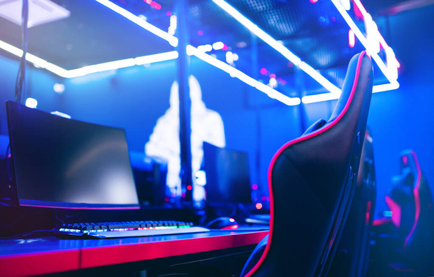 Rozmazané pozadí počítače PC PC, klávesnice křeslo, modré a červené světla. Koncepce online esports arény pro hráče, kteří hrají turnaje - Fotografie, Obrázek