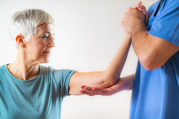 Terapeuta revisando el brazo de las mujeres mayores en la oficina de fisioterapia
  - Foto, Imagen