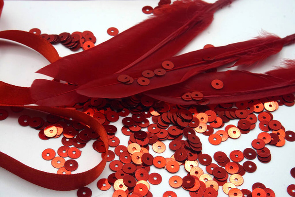Lentejuelas rojas, cinta roja y plumas rojas sobre fondo blanco. Accesorios de costura y decoración utilizados para adornar vestidos
 - Foto, Imagen