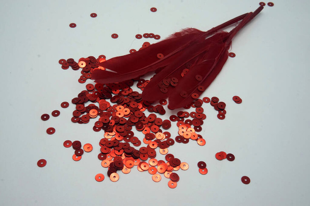 Lentejuelas rojas, cinta roja y plumas rojas sobre fondo blanco. Accesorios de costura y decoración utilizados para adornar vestidos
 - Foto, imagen