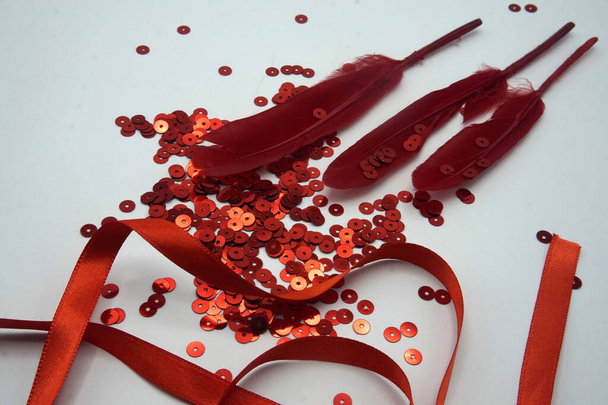 Lentejuelas rojas, cinta roja y plumas rojas sobre fondo blanco. Accesorios de costura y decoración utilizados para adornar vestidos
 - Foto, Imagen