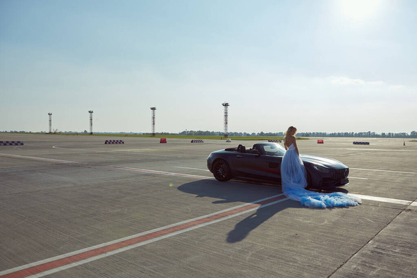 Kyiv, Ukraine - September 2, 2017: The elegant blonde beautiful woman posing near Mercedes Benz AMG GT 50 Edition sports car in airport. A new 2017 supercar designed to celebrate the 50th anniversary - Foto, imagen