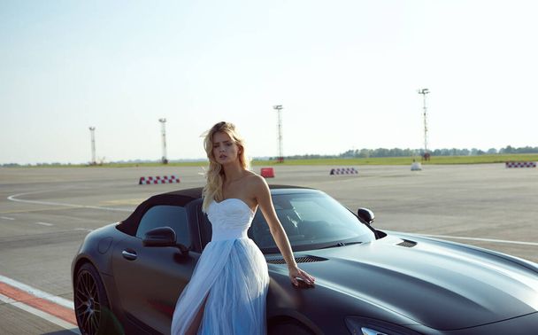Kyiv, Ukraine - September 2, 2017: The elegant blonde beautiful woman posing near Mercedes Benz AMG GT 50 Edition sports car in airport. A new 2017 supercar designed to celebrate the 50th anniversary - Photo, Image