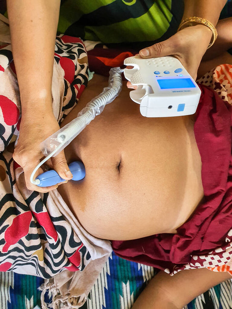 słuchanie dźwięku serca płodu na brzuchu ciężarnej kobiety przy dopplerowskiej maszynie płodu przez wyszkoloną pracownicę służby zdrowia w indiańskim domu - Zdjęcie, obraz
