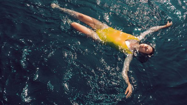 mujer joven en un traje de baño amarillo de una sola pieza flota en la superficie del agua
. - Foto, imagen