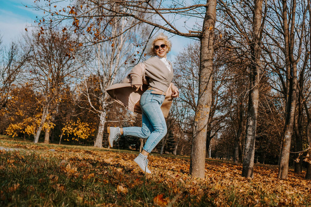 Beautiful woman in autumn park jumping and smiling - Photo, image